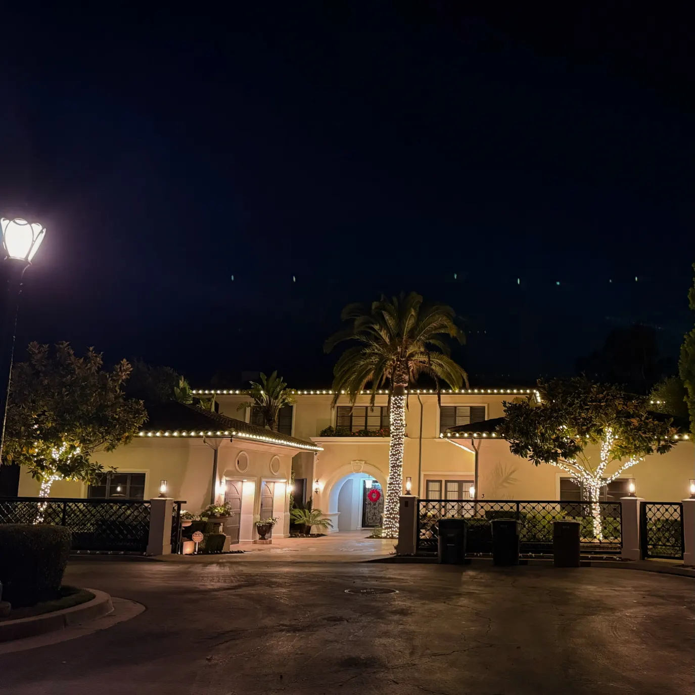 Mediterranean-style home with warm white Christmas lights on the roofline, gate, and palm trees